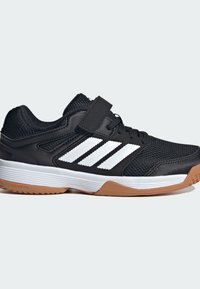 Čierna atletická obuv s mesh vrchom, biele tri pruhy a suchý zips. Obsahuje gumovú podrážku s hnedými detailmi pre lepšiu trakciu.