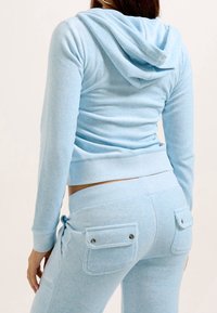 Felpa con cappuccio in cotone azzurro chiaro con cappuccio e maniche lunghe abbinata a pantaloni della tuta coordinati con due tasche posteriori e dettagli in argento.