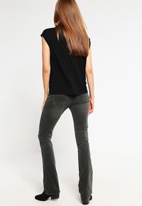Pantalons gris évasés en tissu doux, présentant une texture lisse et des poches discrètes, associés à un haut noir à manches courtes.