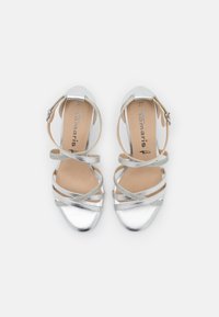 Paire de sandales argentées à brides, boucles à la cheville, bouts arrondis et semelles intérieures beige clair, vues de dessus sur fond uni.