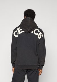 Sort hætte sweatshirt med et stort "CELTICS" trykt i hvidt over ryggen, med en tekstureret finish og rummelig hætte. Enkel design.