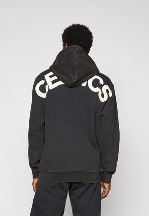 Hoodie noir avec "CELTICS" imprimé en blanc sur le dos, doté d'une finition texturée et d'une capuche spacieuse. Design simple.