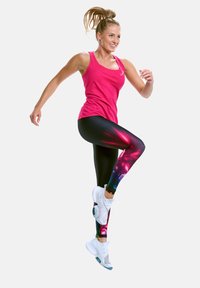 Pink athletic tank top paired with black leggings featuring colorful, abstract patterns. Model wearing white sneakers, in a dynamic pose.