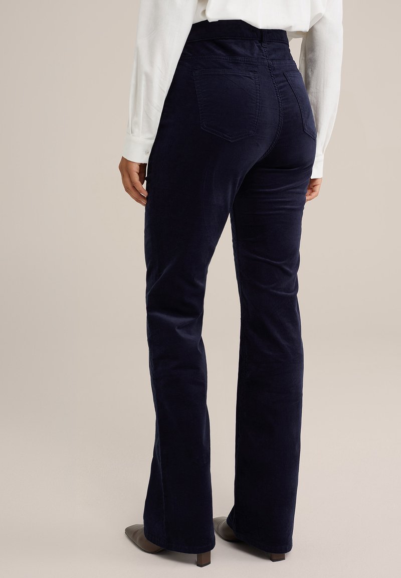 Pantalones de pana en color azul marino con un acabado suave, de tiro alto y con dos bolsillos traseros, combinados con una blusa blanca de manga larga y zapatos marrones.
