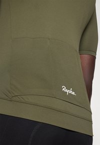 Tricou de ciclism cu mânecă scurtă din material verde olive, având un tiv fără cusături, buzunar pe spate și un logo alb "Rapha" în partea dreaptă jos.