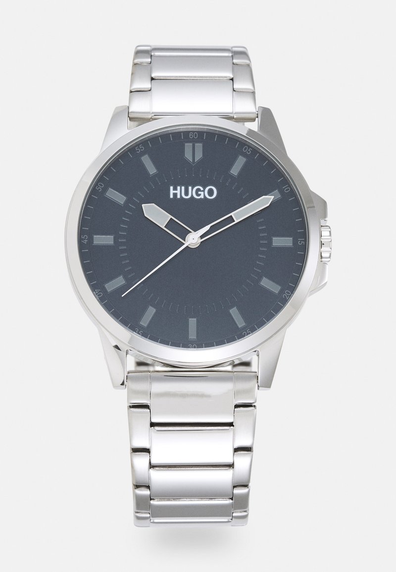 Montre en acier inoxydable argenté avec un cadran gris foncé, logo HUGO, aiguilles argentées et marqueurs d'index sur un bracelet à maillons poli.