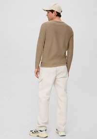 Langarm khaki sweater gemaakt van zachte stof, gecombineerd met witte baggy broek en sneakers. Een beige pet maakt de outfit compleet.