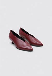 Talons en cuir bordeaux avec un bout pointu et un petit talon. Le design présente une texture lisse et des découpes sur les côtés.