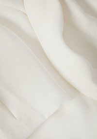 Tissu blanc lisse avec des coutures détaillées et de doux plis, mettant en valeur la texture et le savoir-faire du matériau.