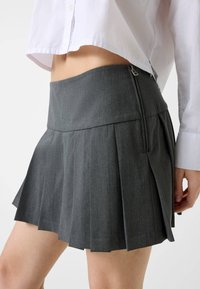 Jupe plissée grise en tissu texturé, avec une taille haute et une fermeture éclair latérale. Longueur courte avec des lignes épurées.