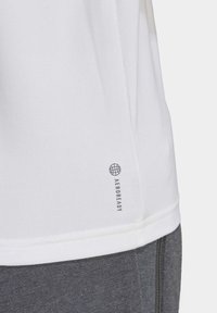 Witte sportshirt met een gladde textuur, voorzien van een donker logo en 'AEROREADY' tekst nabij de onderkant. Draagt over een grijze broek.