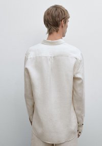 Light beige long-sleeve shirt made of a textured fabric, featuring a pointed collar and buttoned cuffs, with a smooth, casual fit.