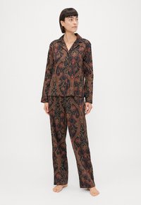 Conjunto de pijama preto com um intrincado padrão floral em vermelho e verde. A parte superior tem um colarinho de lapela e mangas compridas; as calças têm corte reto.