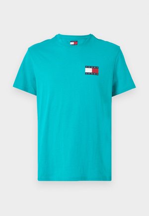 Turkos bomullströja med korta ärmar, med en liten flerfärgad logopatch på vänster bröst. Klassisk rund halsringning.