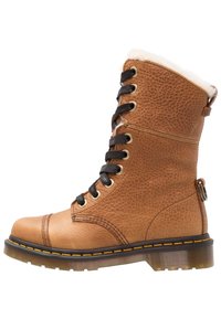 Botas de cuero marrón con cordones, acabado texturizado, cordones negros, cuello de piel sintética y suela de goma resistente con detalles de costura amarilla.