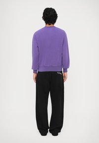 Lilla sweatshirt med lange ærmer, ribbede manchetter og kant. Kombineret med løse sorte bukser med et hvidt logo på ryggen.
