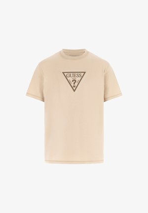 Camiseta de algodón color beige con mangas cortas, con un logo triangular de 'GUESS' en tonos más oscuros en el frente, textura suave y cuello redondo.