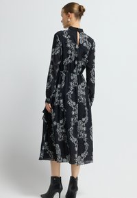 Zwarte lange mouwen jurk met witte paisleyprint, strakke taille en sleutelgatdetail op de rug. Gecombineerd met zwarte enkellaarzen.