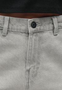 Svetlosivé džínsy so zapínaním na zips a gombík, s pútkami na opasok a rovnými nohavicami. Viditeľné švy a hladká textúra.