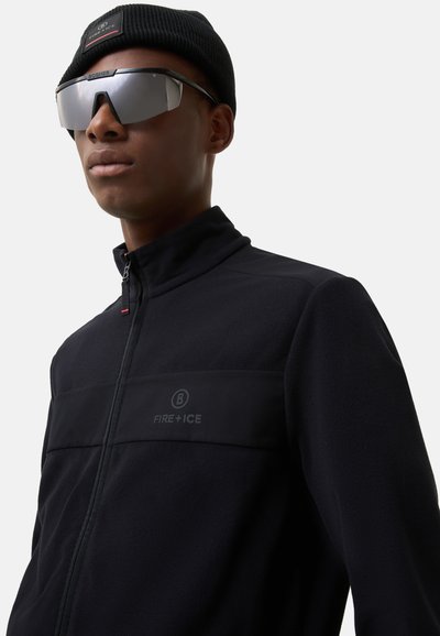 Black fleece jacket with high collar and zip, featuring a textured panel labeled "FIRE+ICE." Accompanied by a black beanie and mirrored sunglasses.