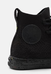 Zwarte gebreide hoge sneaker met een gemêleerde stof, rubberen zool en een ronde logopatch met een ster ontwerp aan de zijkant.