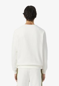 Sudadera de forro polar blanco con cuello redondo, puños y dobladillo acanalados, que presenta una textura suave y un corte holgado.