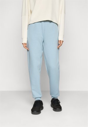 Svetlomodré tepláky so zúženým strihom a rebrovanými manžetami, v kombinácii so smotanovým sveterom. Čierne športové topánky dotvárajú outfit.