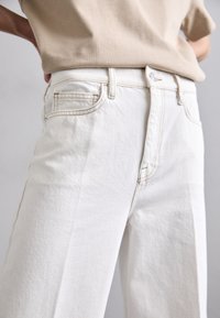 Jeans de mezclilla blanca con un corte recto, que presentan un frente limpio, bolsillos estándar y detalles de costura ligera. Tejido de algodón texturizado.