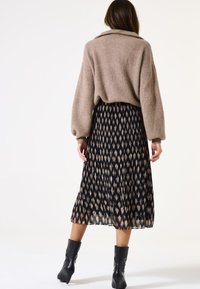 Beige geribbeld sweater met verlaagde schouders, gecombineerd met een zwarte geplooide rok met een lichtbruine abstracte print. Zwarte enkellaarzen maken de look af.