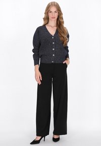 Marineblauwe, sprankelende brei cardigan met een v-hals, zes knopen en verlaagde schouders, gecombineerd met zwarte hoge taille brede broek en hakken.
