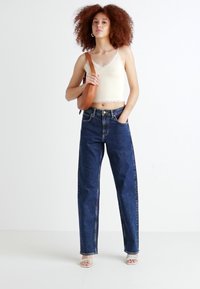 Vaqueros de mezclilla en azul oscuro con cintura alta y piernas rectas, combinados con una camiseta sin mangas color crema y un bolso de hombro marrón.