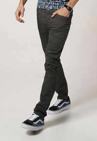 Donkergrijze slim-fit broek met een gladde textuur, gecombineerd met marineblauwe en witte sneakers met een klassiek ontwerp en contrasterende accenten.