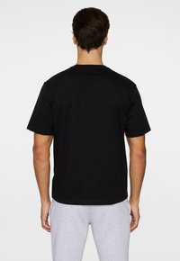 T-shirt en coton noir à manches courtes, col rond et coupe droite. Tissu texturé avec une apparence lisse, sans motifs visibles.