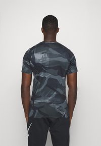 Camisa de manga corta con patrón de camuflaje oscuro y corte ajustado, hecha de material elástico. Cuenta con un cuello de canalé y la marca "NIKE PRO".