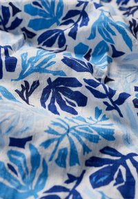 Tessuto di cotone con un motivo floreale, caratterizzato da foglie blu scuro e blu chiaro su uno sfondo bianco, che mette in evidenza texture e profondità.