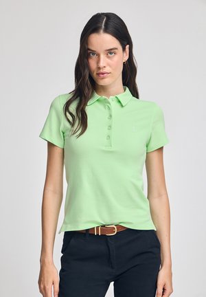 Polo shirt verde chiaro realizzato in morbido cotone. Presenta un colletto, una patta con bottoni e un logo discreto sul petto. Indossato con pantaloni scuri e una cintura.