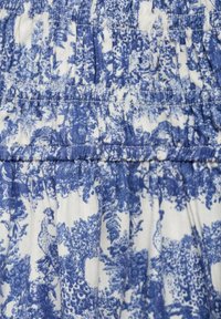 Blauwe en witte bloemenstof met geplooide textuur en elastische tailleband, met een bedrukt ontwerp van gestileerde planten en pauwen.