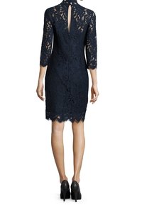 Femme portant une robe en dentelle bleu marine arrivant aux genoux avec des manches trois-quarts et des chaussures à talons noirs, vue de dos.