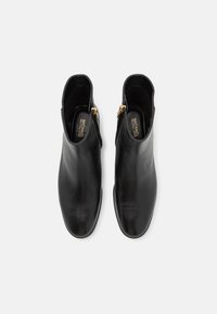 Botas de cuero negro hasta el tobillo con una textura suave, punta redonda y cremallera lateral con herrajes dorados. Branding sutil visible en la plantilla.