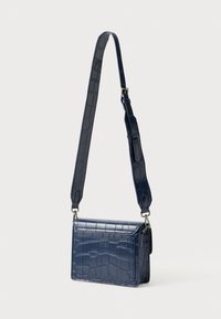 Tumesinine õlakott, mis on valmistatud reljeefsest kunstkrokodillinahast. Ristkülikukujuline kuju, reguleeritava rihmaga ja hõbedaste detailidega.