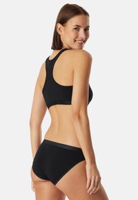 Musta puuvillainen bralette, jossa on urheilullinen selkäosa, yhdistettynä matching korkeavyötäröisiin alusvaatteisiin. Molemmissa on pehmeä rakenne ja minimaalinen brändäys.