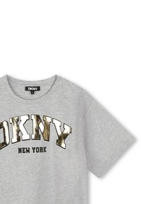 Camiseta de algodón gris con mangas cortas, que presenta letras en negrita de color dorado metálico "DKNY" sobre "NEW YORK" en negro. Cuello redondo.
