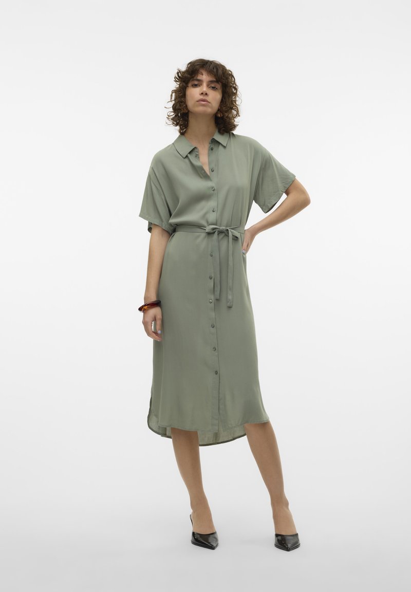 Robe verte olive à boutons, à manches courtes, avec une taille cintrée par une ceinture et une longueur mi-mollet. Tissu lisse avec un léger éclat.