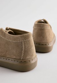 Bruna mockaskor med rund tå och kort ankelhöjd. Har en texturerad gummisula och sömdetaljer längs kanten.