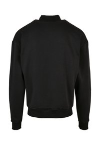Sudadera negra con cuello redondo, mangas largas y puños de canalé. Textura suave, corte holgado y diseño simple sin detalles adicionales.