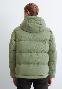 Veste matelassée verte avec capuche, présentant un design matelassé, des poignets élastiques et une texture lisse. La vue de dos ne montre aucun logo visible.