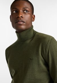 Maglione a collo alto verde oliva realizzato in morbido tessuto a maglia, con un logo in rilievo sul petto e un design aderente.