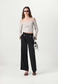 Off-the-shoulder beige top with twisted detail, paired with high-waisted black wide-leg trousers featuring double silver buttons and black straps.