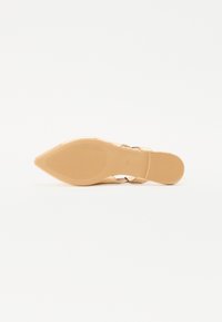 Chaussure à talon haut beige avec un bout pointu, un dessus lisse et une fine bride de cheville. La semelle présente un motif de grip texturé.