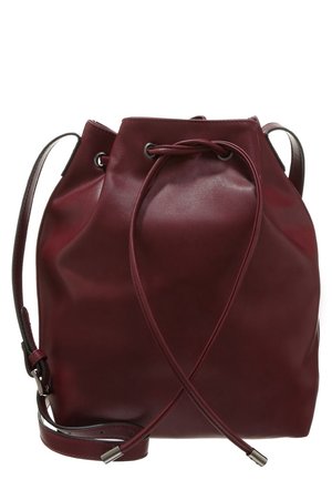 Tmavě červená kbelíková kabelka z kůže s nastavitelným ramenním popruhem a zatahovacím uzávěrem s kovovými průchodkami a koncovkami.